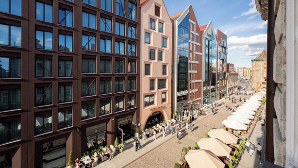 A modern building with multiple floors, large windows, and a ground-level outdoor seating area with umbrellas. - Stągiewna Old Town Apartment (Gdańsk)