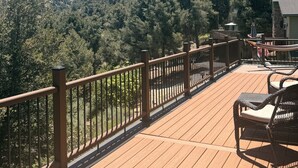 A wooden deck with a railing, overlooking a forested hillside.