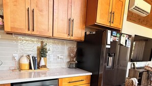A kitchen with wooden cabinets, a black refrigerator, a dishwasher, and a countertop with various items.