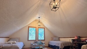A cozy attic bedroom with two beds, a dining table, and a chandelier.