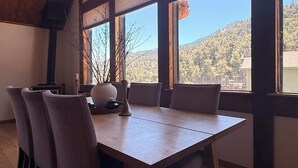 A dining area with a wooden table and chairs, large windows with a view of a forested hillside.