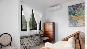 Une chambre à coucher comprenant un lit, une chaise, un bureau, une commode et une fenêtre avec des rideaux.