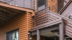 Un bâtiment moderne avec un revêtement en bois, une clôture en verre et un petit jardin agrémenté d’une fontaine circulaire.