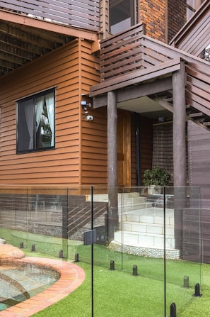 Un edificio moderno con rivestimento in legno, recinzione in vetro e un piccolo giardino con elemento d'acqua circolare.