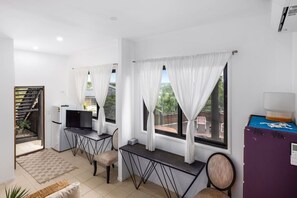 A room with a desk, chair, TV, and windows with curtains.
