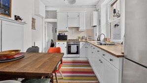 A kitchen with white cabinets, a wooden table, and a colorful striped rug. - Stylish Two Bedroom Apartment (London)