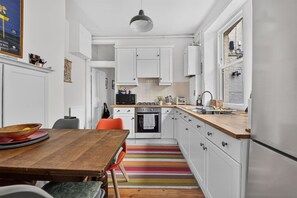 A kitchen with white cabinets, a wooden table, and a colorful striped rug. - Stylish Two Bedroom Apartment (London)