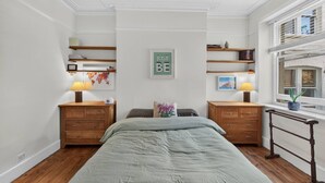 A bedroom with a bed, two nightstands, a wall-mounted shelf, a window with a view, and a 'JUST BE' sign. - Stylish Two Bedroom Apartment (London)