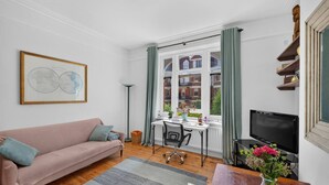 A living room with a sofa, a desk, a chair, a TV, and a window with curtains. - Stylish Two Bedroom Apartment (London)