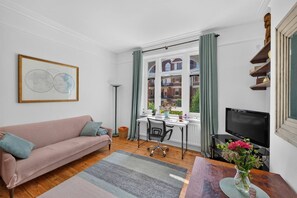 A living room with a sofa, a desk, a chair, a TV, and a window with curtains. - Stylish Two Bedroom Apartment (London)