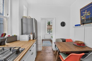 A compact kitchen with a refrigerator, a sink, and a dining area with chairs. - Stylish Two Bedroom Apartment (London)
