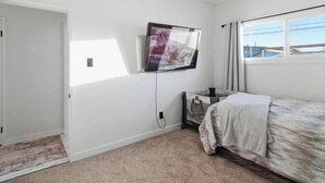 Een slaapkamer met een bed, een aan de muur bevestigde televisie, een raam met gordijnen en een deur.