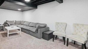 Een kamer met een grijze hoekbank, een witte salontafel en twee witte fauteuils.