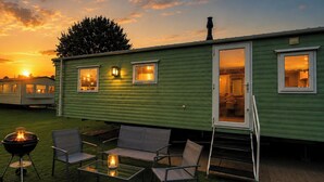 Une caravane verte avec un espace patio comprenant un barbecue, des chaises et une table avec un chandelier.