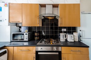 A compact kitchen with a microwave, toaster, kettle, and a stove. - Stylish 2 Bedroom with Free Parking (Manchester)