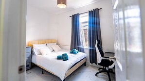 Ein Schlafzimmer mit Bett, Nachttisch, Stuhl und einem Fenster mit Vorhängen.