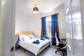 A bedroom with a bed, bedside table, chair, and a window with curtains. - Stylish 2 Bedroom with Free Parking (Manchester)