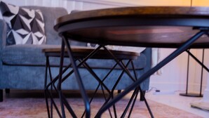 Ein runder Tisch mit Metallgestell, eine Couch mit Kissen in geometrischem Muster und eine Lampe im Hintergrund.