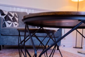 A round table with a metal frame, a sofa with a geometric-patterned cushion, and a lamp in the background. - Stylish 2 Bedroom with Free Parking (Manchester)
