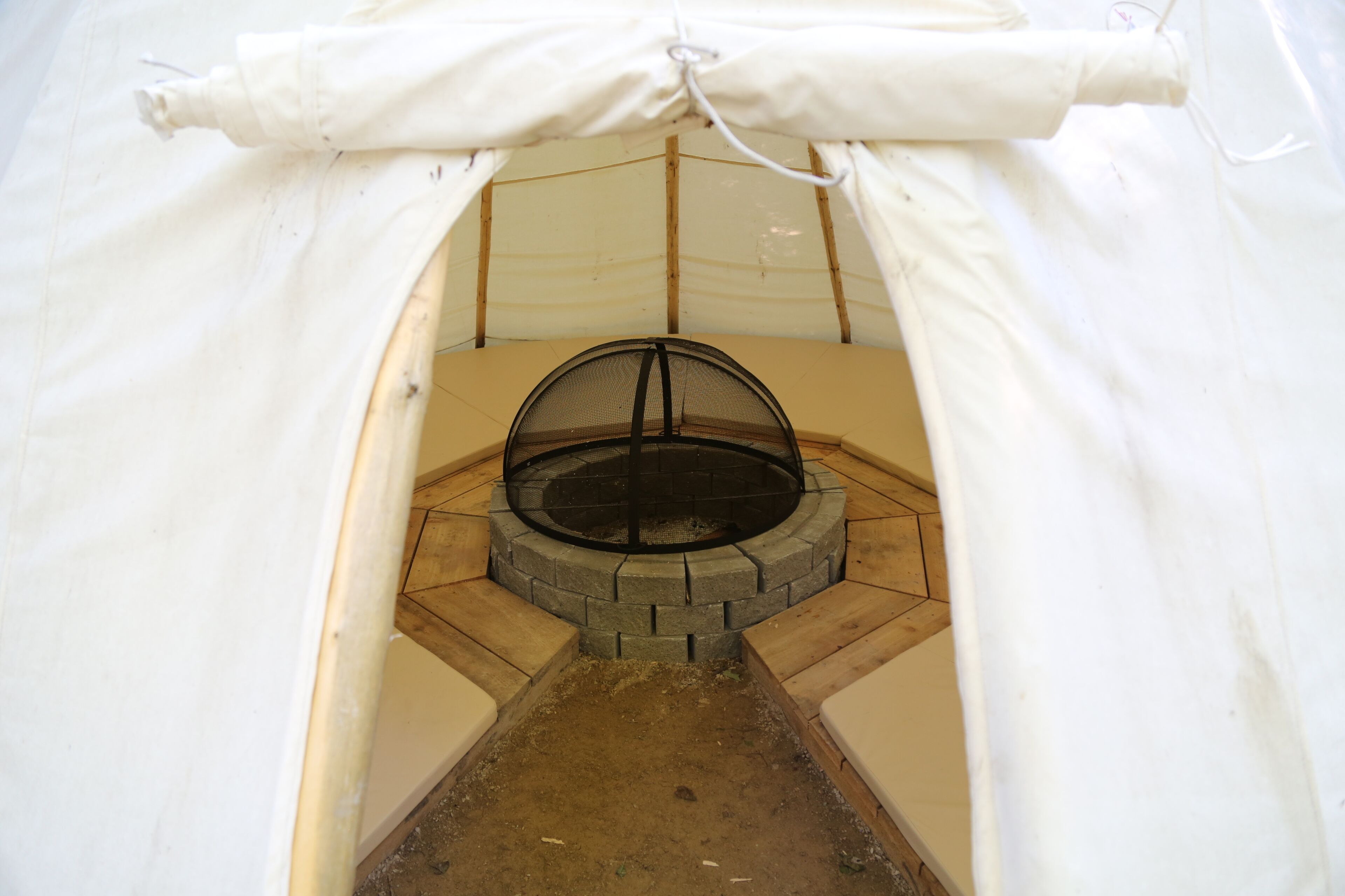 A tent with a circular stone fire pit and a white canopy.