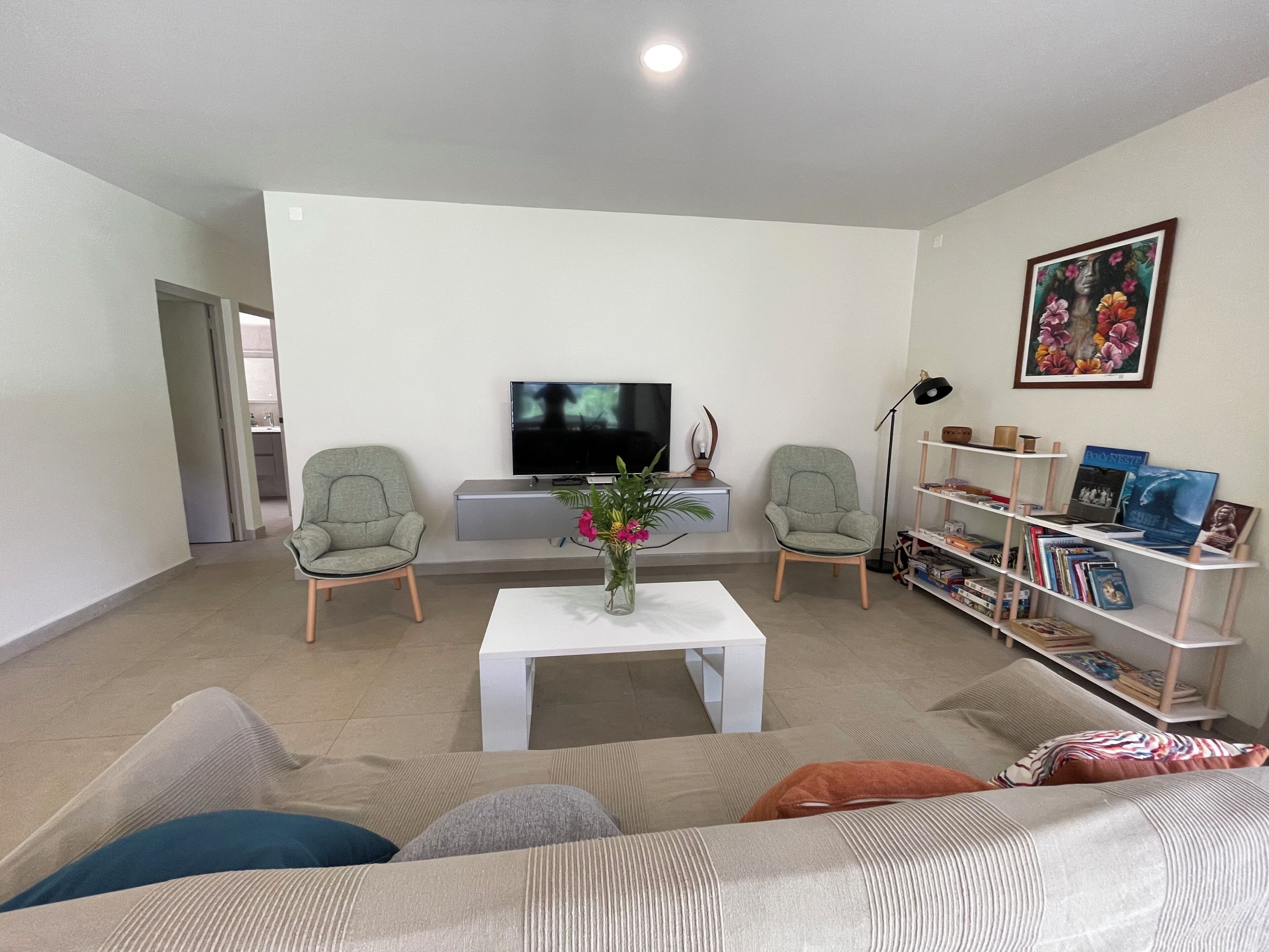 Un salon comprenant un téléviseur, deux fauteuils, une table basse, une bibliothèque et un tableau accroché au mur.