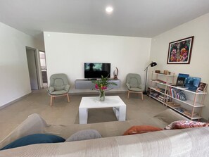 Ein Wohnzimmer mit Fernseher, zwei Sesseln, einem Couchtisch, einem Bücherregal und einem Bild an der Wand.