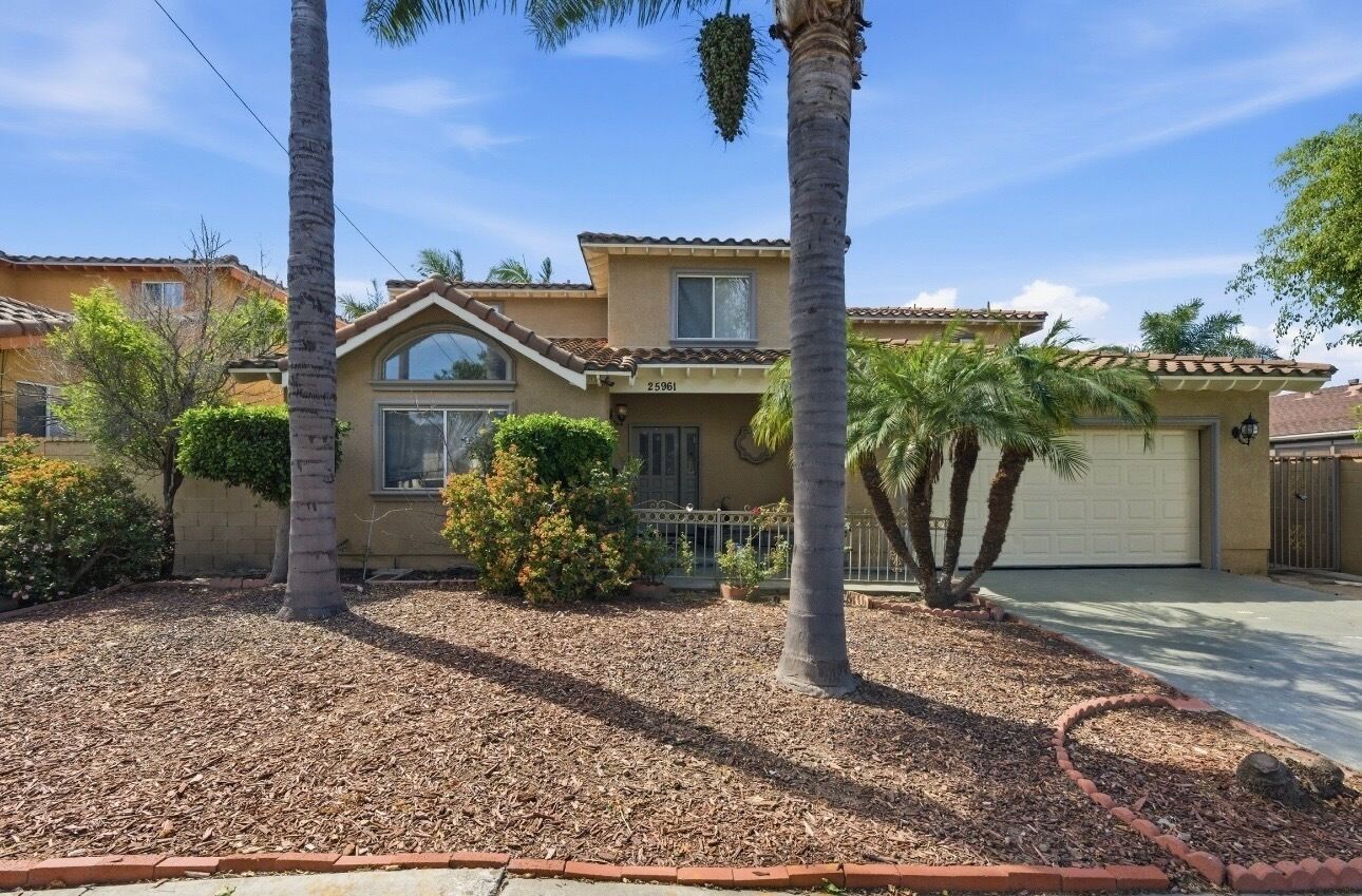 A two-story house with a garage, surrounded by palm trees and a well-maintained garden.