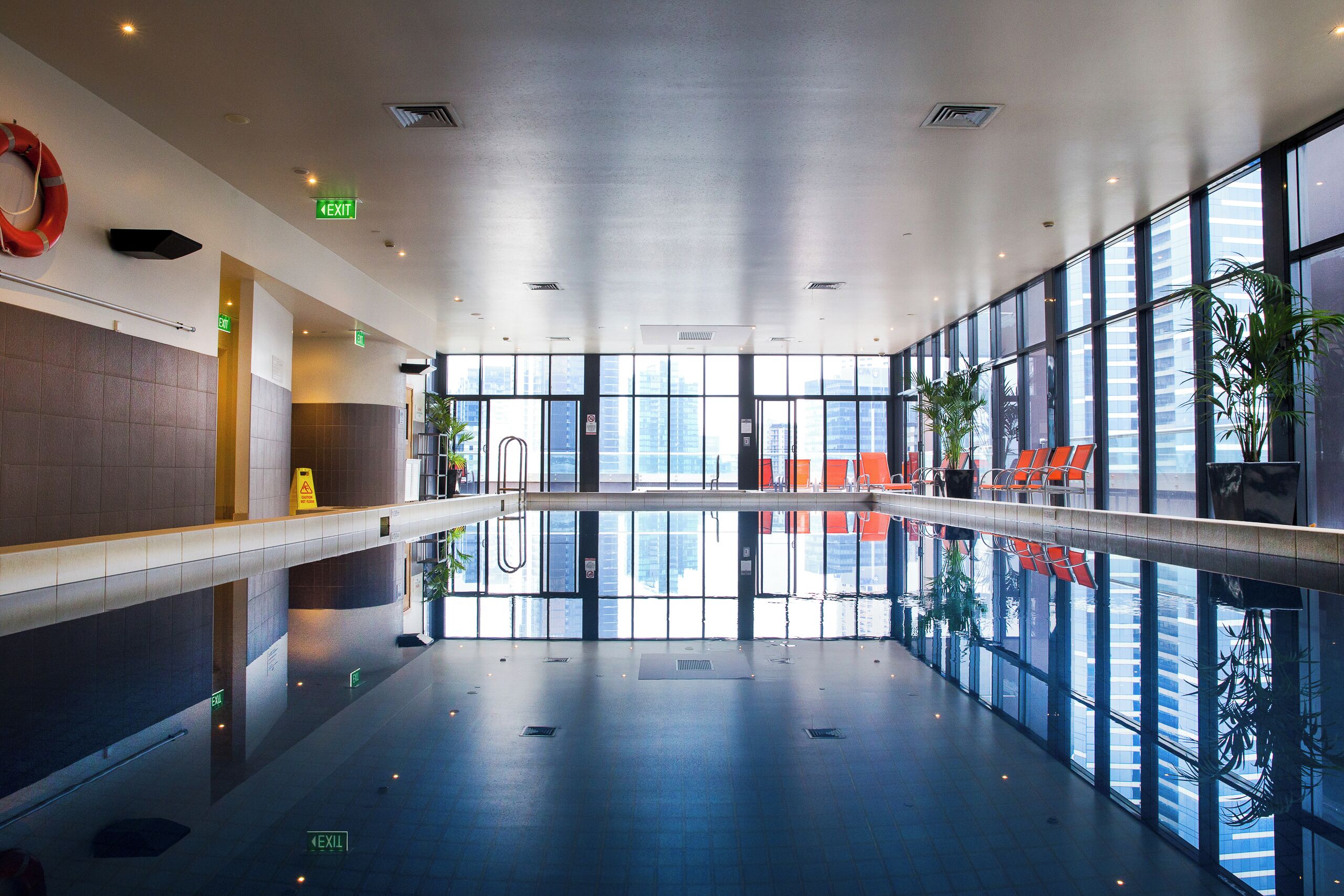 A spacious indoor area with a reflective floor, large windows, and exit signs.