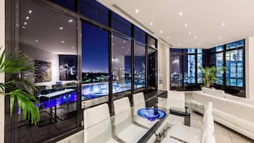A modern interior with a glass table, white chairs, and a view of a cityscape at night.
