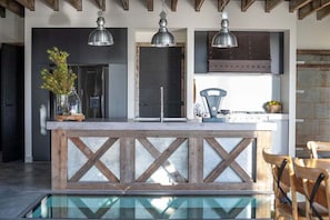 A modern kitchen with a central island, pendant lights, and a view of the outdoors.
