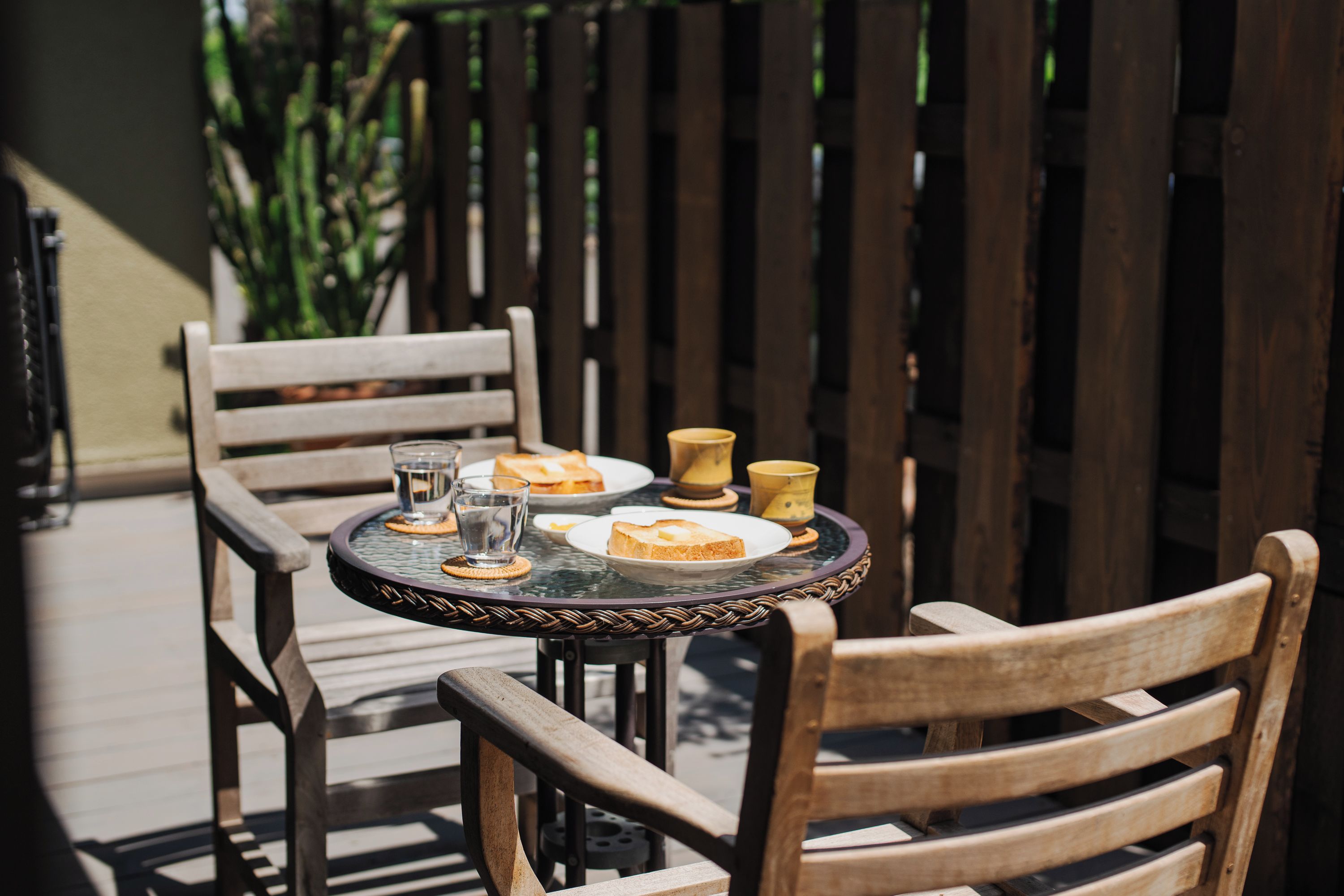 Une table ronde avec un plateau en verre, entourée de chaises en bois, sur laquelle on trouve des assiettes de nourriture et des verres d’eau.