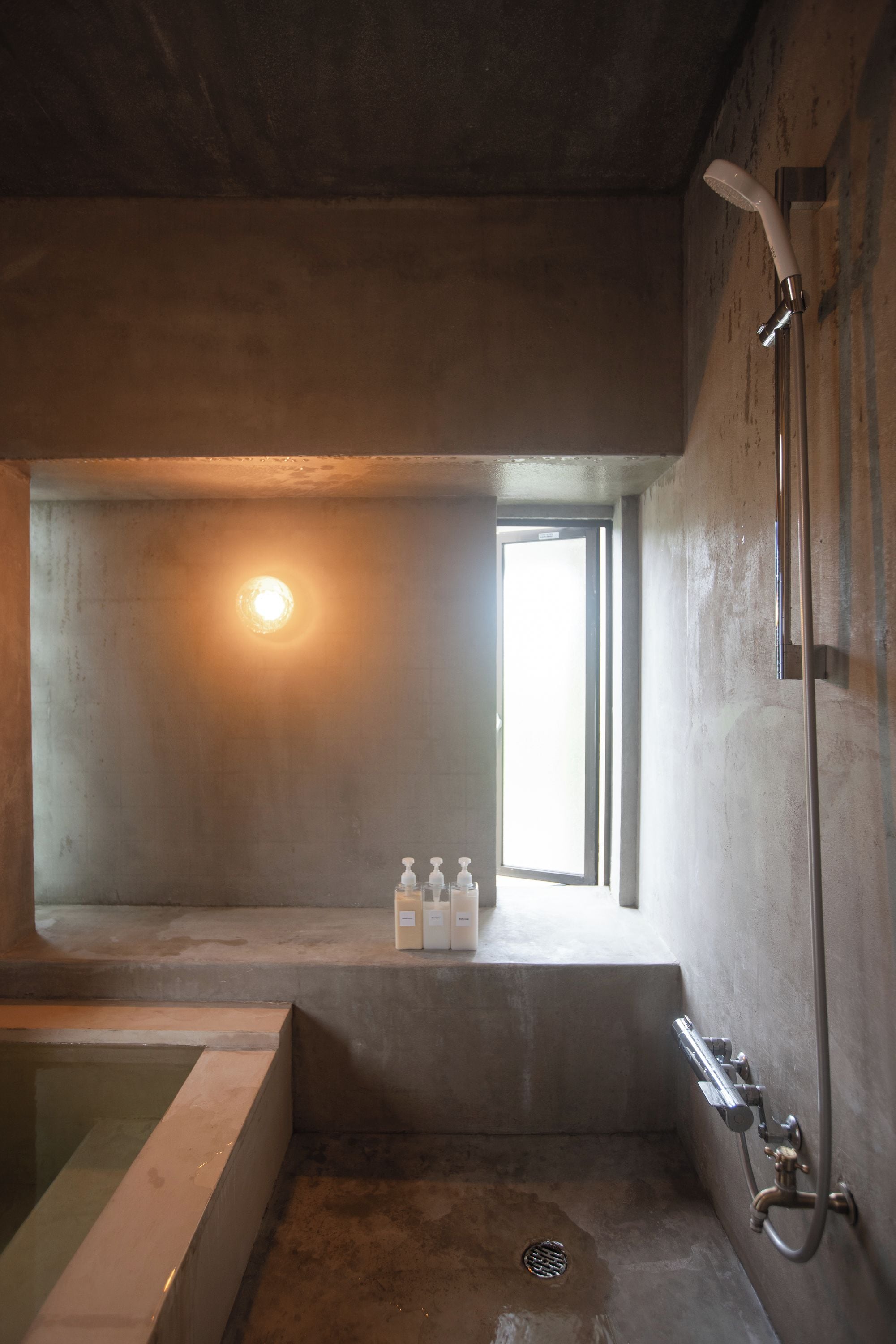 Une salle de bain minimaliste avec une baignoire, une douche et une fenêtre qui laisse entrer la lumière naturelle.