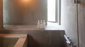 Une salle de bain minimaliste avec une baignoire, une douche et une fenêtre qui laisse entrer la lumière naturelle.