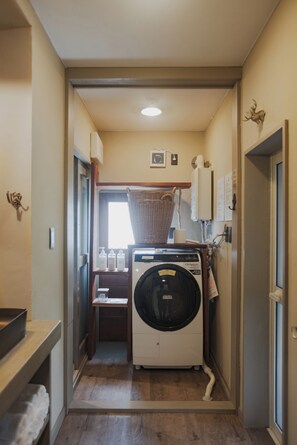 A laundry room with a front-loading washing machine, a drying rack, and a small table with bottles. - ROHAUS: Entire Home with Private Hot Spring (白老町)