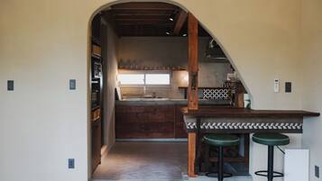 Une cuisine avec une arche donnant sur un coin repas, des tabourets de bar en bois et un four encastré.