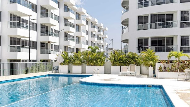 A modern hotel with a swimming pool, outdoor seating, and a white facade. - Apto moderno en Serena con balcon  (Cartagena)