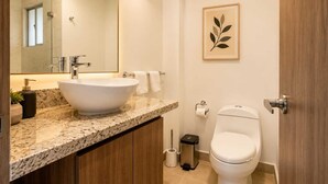 A bathroom with a marble countertop, a vessel sink, a toilet, a trash bin, and a framed leaf artwork. - Apto moderno en Serena con balcon  (Cartagena)