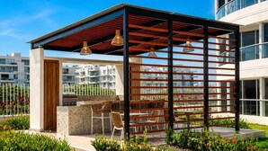 A rooftop patio with a grill, seating, and a pergola with hanging lights. - Apto moderno en Serena con balcon  (Cartagena)