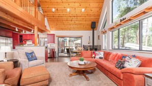 A spacious living area with a fireplace, a kitchen with red cabinets, and large windows offering a view of the outdoors. - Cozy Mountain Retreat, 5 Min Walk to  Downtown, Lake Membership, Sleeps 7 (Twain Harte)