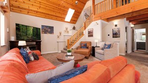 A spacious living room with a wooden ceiling, a large flat-screen TV, a staircase, and a cozy seating area with a sofa and armchairs. - Cozy Mountain Retreat, 5 Min Walk to  Downtown, Lake Membership, Sleeps 7 (Twain Harte)