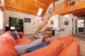 A spacious living room with a wooden ceiling, a large flat-screen TV, a staircase, and a cozy seating area with a sofa and armchairs. - Cozy Mountain Retreat, 5 Min Walk to  Downtown, Lake Membership, Sleeps 7 (Twain Harte)