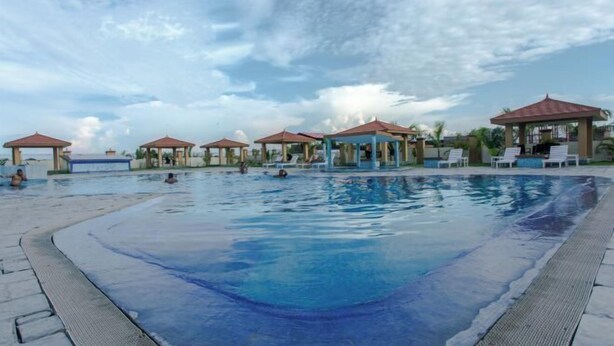 A swimming pool with lounge chairs and gazebos, surrounded by a clear sky. - Bodhi Redsun (Rupandehi)