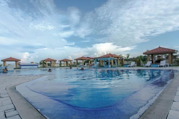 A swimming pool with lounge chairs and gazebos, surrounded by a clear sky.