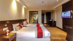 A hotel room with two beds, a TV, and a desk with a lamp. - Bodhi Redsun (Rupandehi)