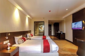 A hotel room with two beds, a TV, and a desk with a lamp.