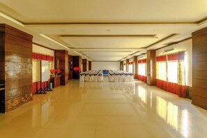 A long, narrow hotel corridor with rows of tables and chairs, wooden paneling on the walls, and large windows with curtains.