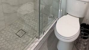 Et badeværelse med brusekabine i glas, toilet og gulv med sekskantede fliser.