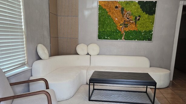 A living room with a sectional sofa, a coffee table, a chair, a painting on the wall, and a ceiling fan. - Free Parking near Cowboy Stadium (Arlington)