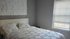 A bedroom with a bed, a headboard, a window with blinds, and a wall with a geometric pattern. - Free Parking near Cowboy Stadium (Arlington)