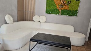 A modern living room with a sectional sofa, a black coffee table, a textured rug, a wall-mounted abstract art piece, and a ceiling light fixture. - Free Parking near Cowboy Stadium (Arlington)